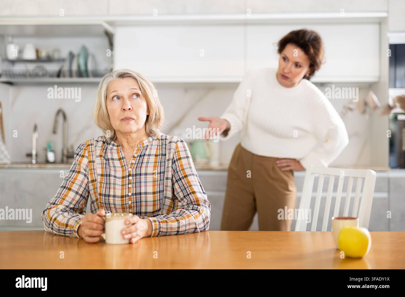Sconvolta la vecchia seduta al tavolo della cucina con le spalle a donna che litigano con lei Foto Stock