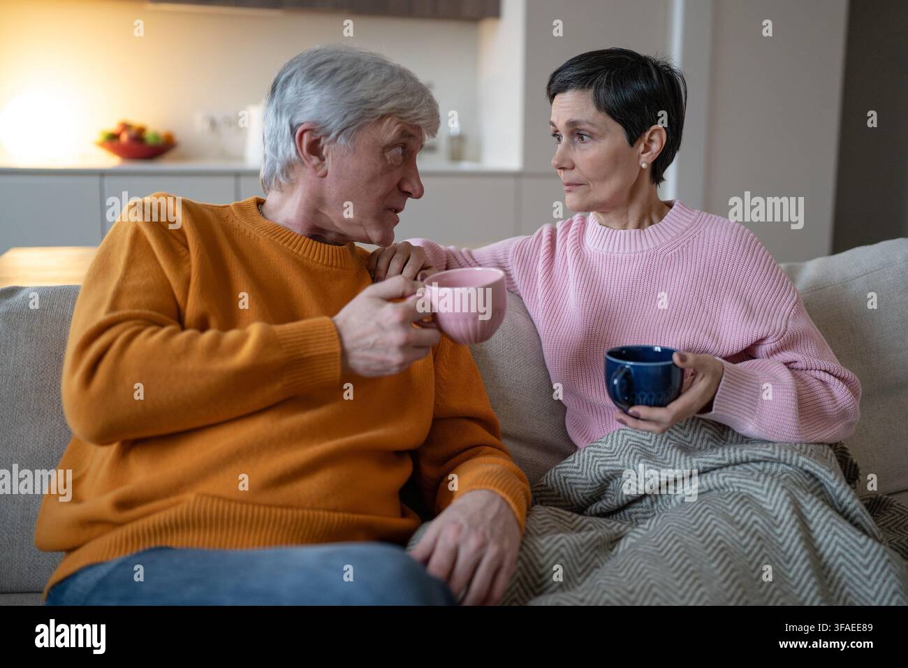 Moglie pensierosa che ascolta il marito anziano mentre la coppia sposata si rilassa insieme a casa sul divano. Foto Stock