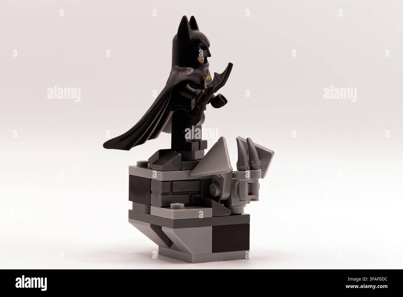 Minifigura Lego Batman in piedi su un cornicione di gargoyle in pietra grigia che tiene un'arma batarang. Foto Stock