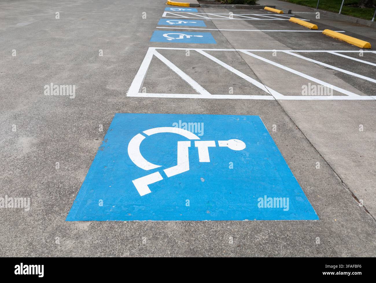 Diverse posti auto accessibili segnalati con simboli blu di sedia a rotelle e corsie di accesso a strisce in un'area di parcheggio vuota. Foto Stock