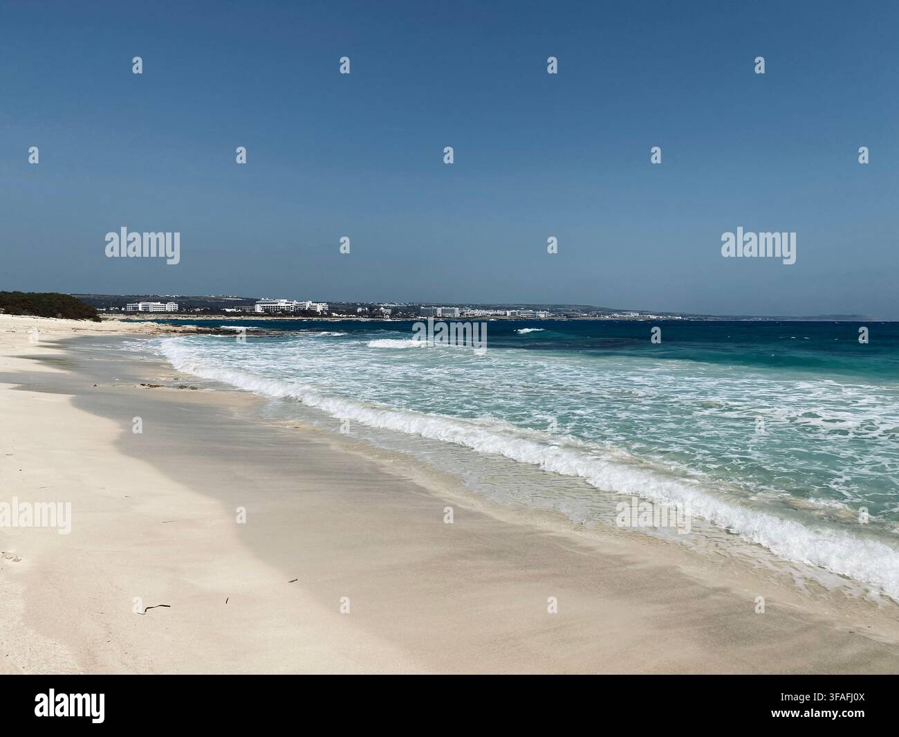 Onde chiare di colore blu-verde si infrangono su un'ampia distesa di sabbia bianca sotto un cielo blu aperto. - Immagine stock catturata con smartphone