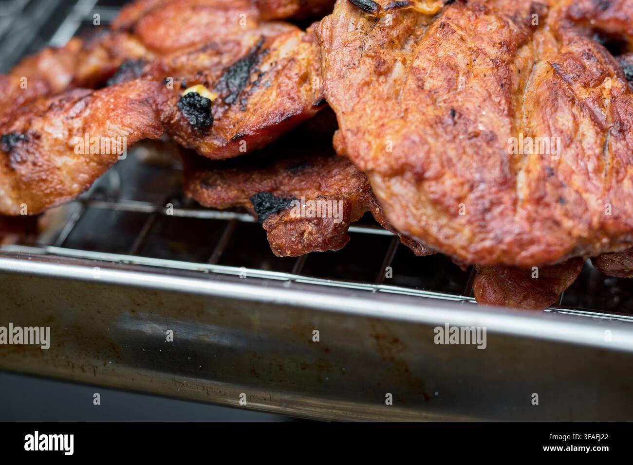 Bistecche di maiale marinate succose appena grigliate su una griglia a filo da barbecue con una crosta dorata appetitosa, fumo di carbone delicato e carne tenera Foto Stock
