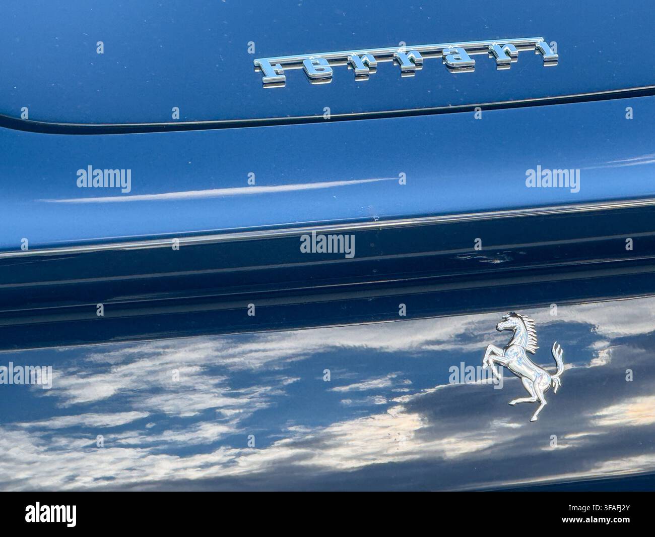 Riga, Lettonia – 19 agosto 2026: Primo piano di un emblema Ferrari cromato e delle scritte riflesse sulla carrozzeria blu lucida di un'automobile sportiva di lusso, hig Foto Stock