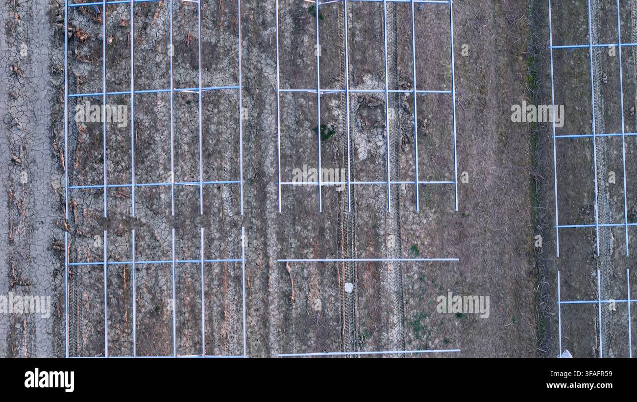 Impianto solare in sviluppo aereo nella Val Padana che installa strutture di montaggio per pannelli fotovoltaici, rappresentando l'espansione delle energie rinnovabili e il te verde Foto Stock