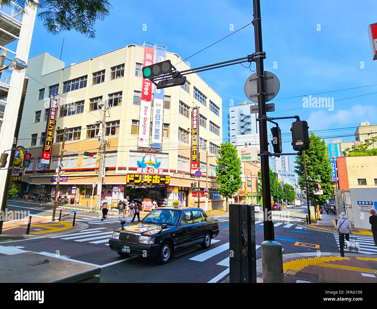 Taxi nero classico che attraversa un incrocio vicino al negozio Don Quijote a Fujisawa, Giappone - Immagine stock catturata con smartphone