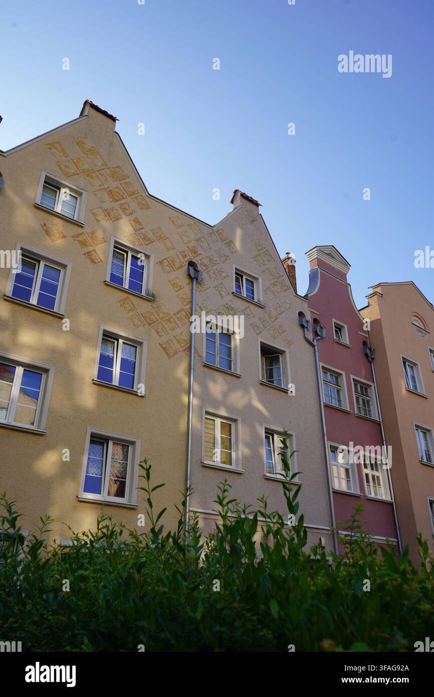La luce del sole e le ombre degli alberi si proiettano sulle facciate degli edifici decorati con sgraffito nel quartiere storico della vecchia città di Danzica, viste dietro cespugli verdi frondosi Foto Stock