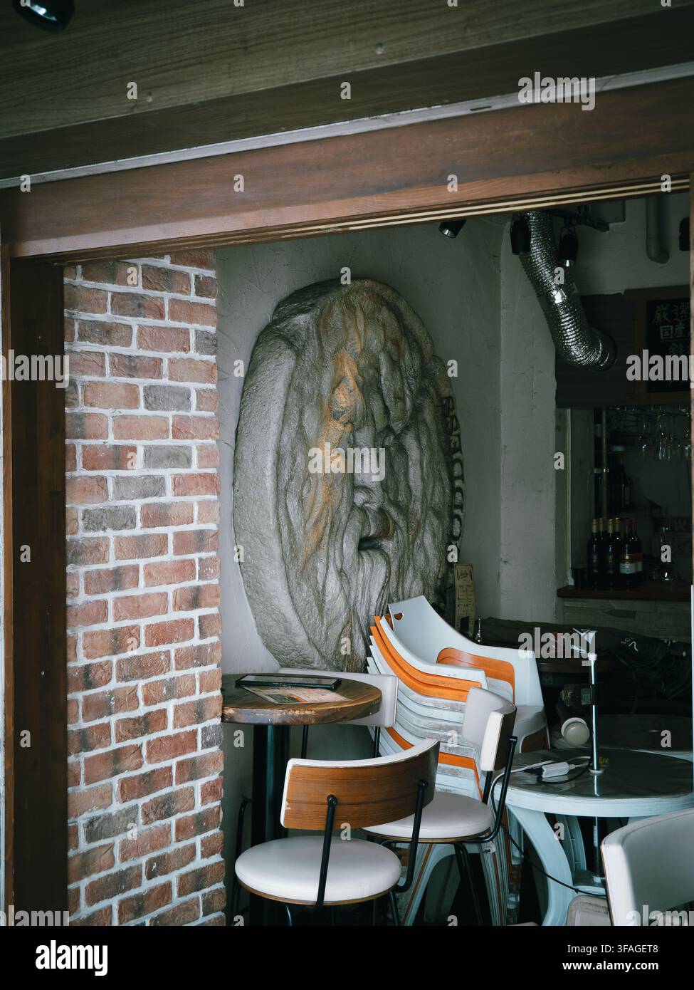 Grande scultura in pietra di un volto sulla parete di un interno di bar con muri in mattoni e mobili moderni a Osaka, Giappone Foto Stock