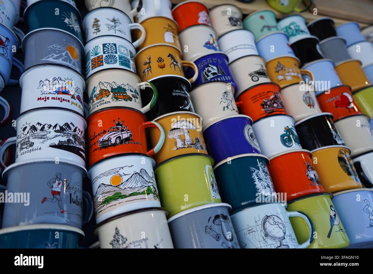 File di tazze smaltate illustrate e colorate in vendita, con vari disegni come paesaggi, animali e testi, su uno stand di mercato affollato. Foto Stock