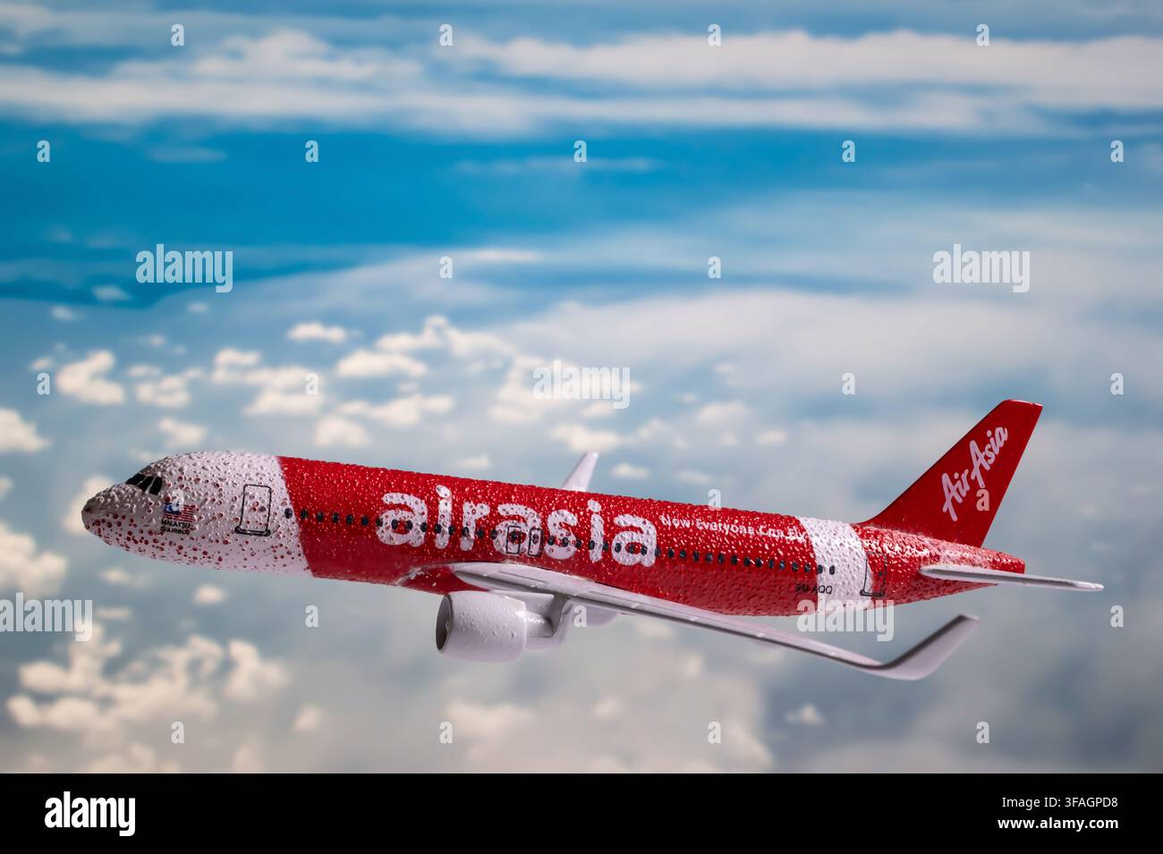 Chiang Mai, Thailandia - 7 agosto 2026 : Modello di aereo in metallo pressofuso con livrea rossa AirAsia coperto di gocce d'acqua che vola sopra le nuvole bianche Foto Stock