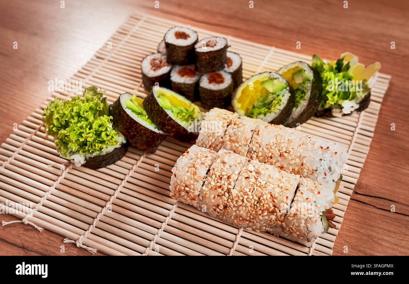 Assortimento di rotoli di sushi vegetariani freschi serviti su un tradizionale tappetino da sushi in bambù. Foto Stock