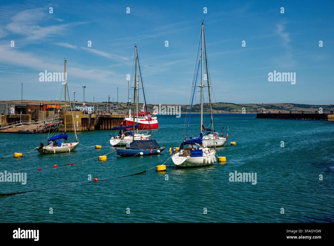 Yacht ormeggiati nell'acqua blu di un porto con l'imboccatura che dà accesso al mare e alla costa oltre, Weymouth, Dorset, Inghilterra. Foto Stock