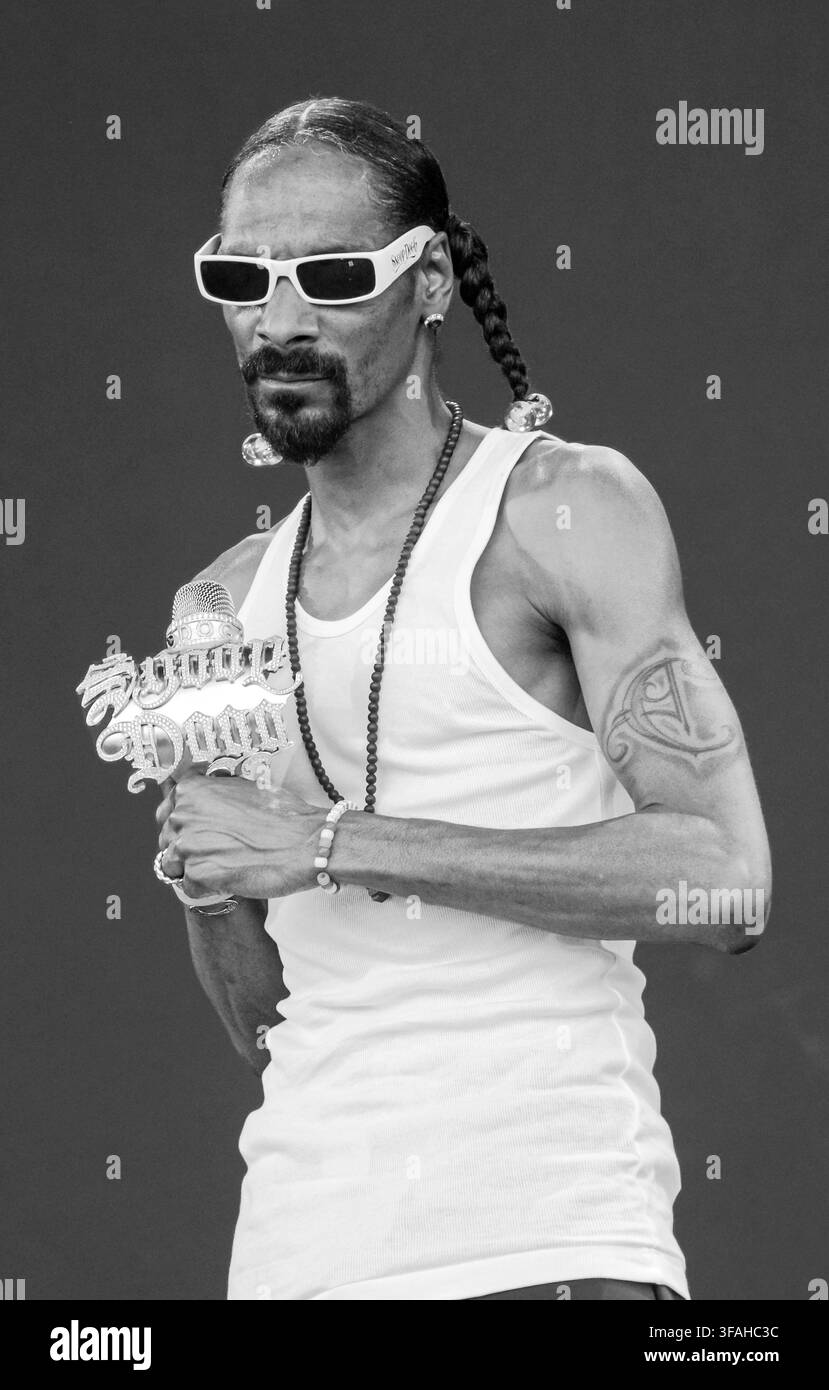Un ritratto in bianco e nero del rapper Snoop Dogg che tiene un microfono personalizzato tempestato di gioielli, con occhiali da sole, una canottiera bianca e capelli intrecciati. Foto Stock