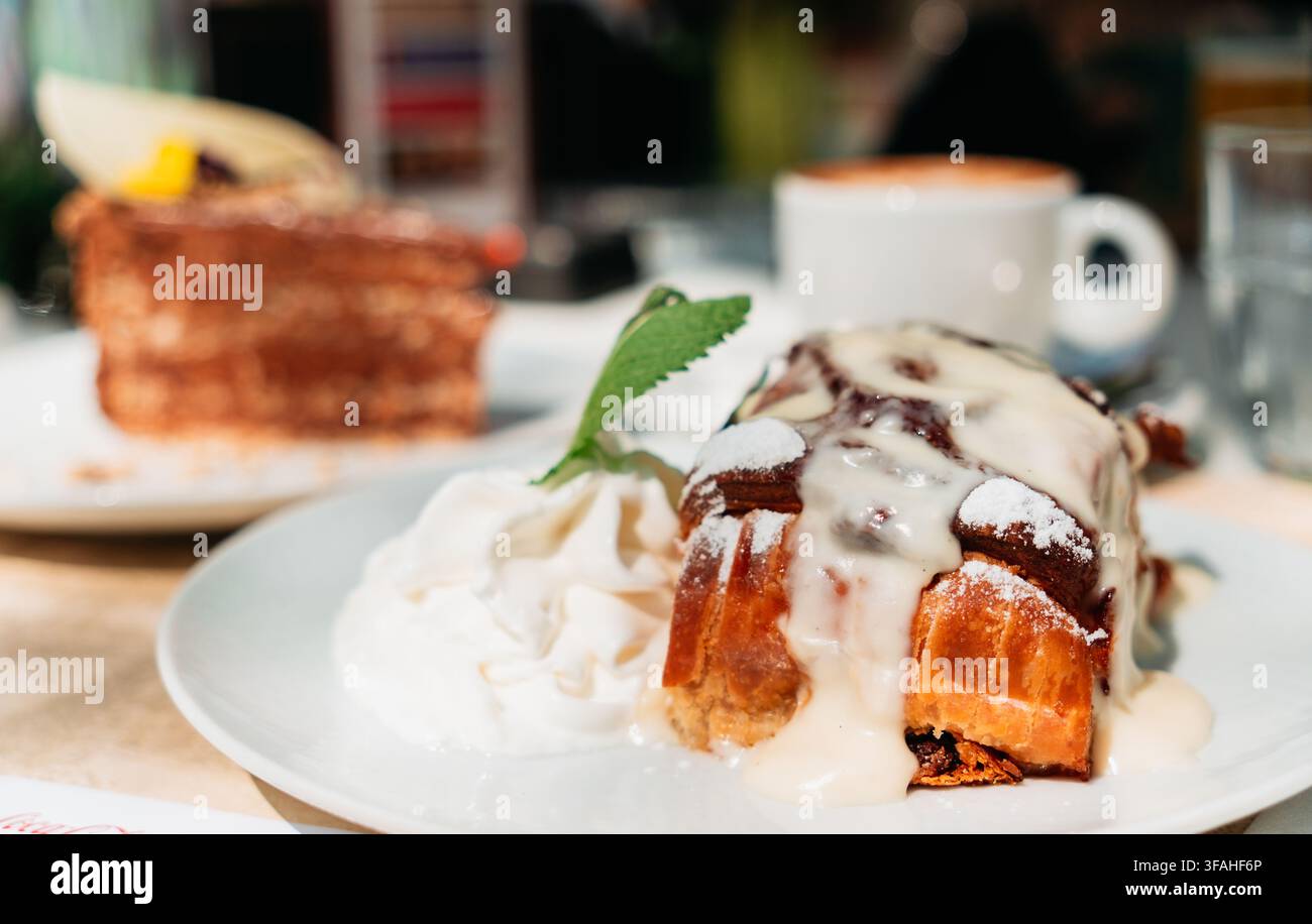 Strudel dorato servito con panna montata e salsa alla vaniglia su un piatto luminoso. La consistenza calda della pasta e l'elegante presentazione del dessert creano una dolcezza accogliente Foto Stock