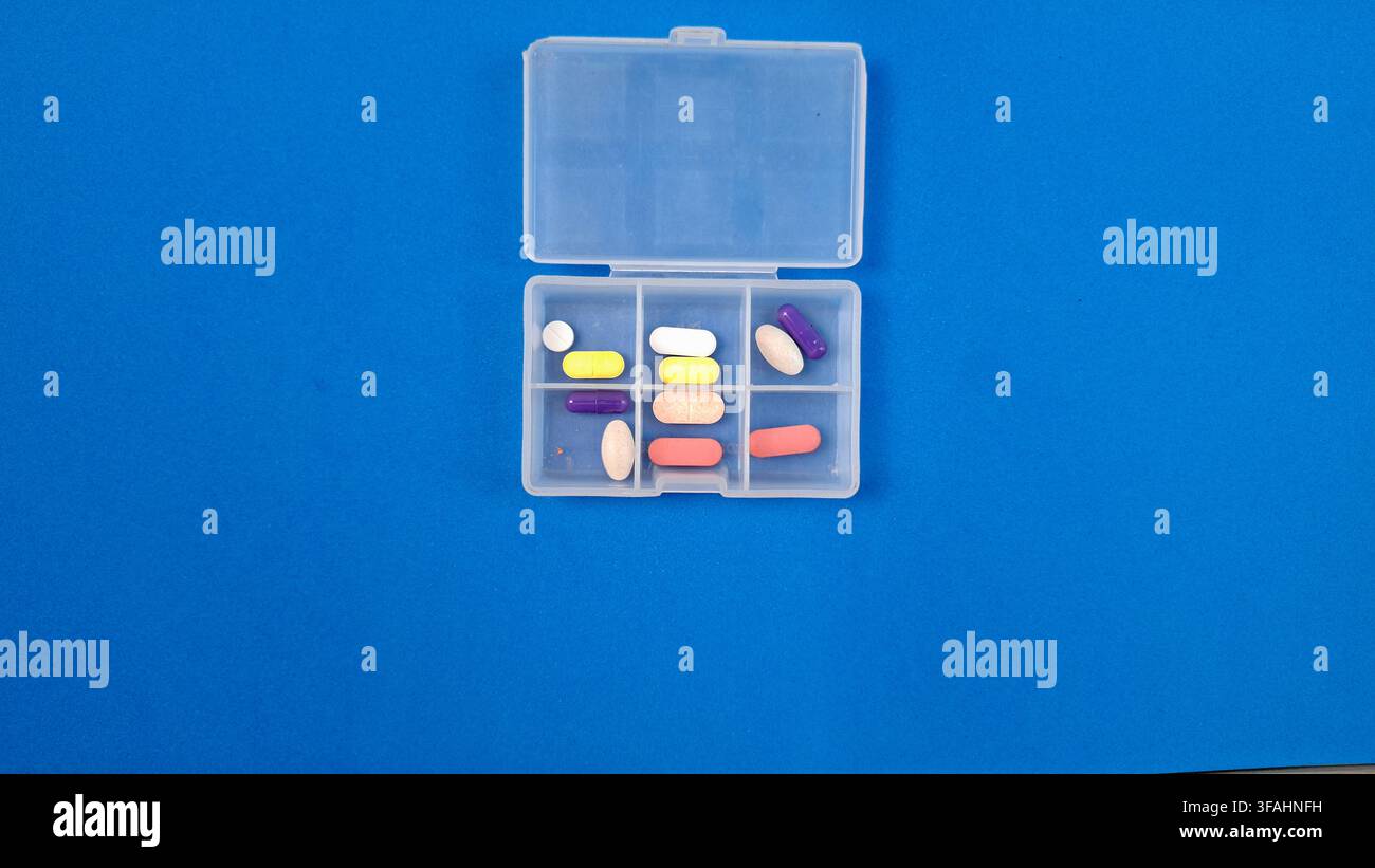 Organizer per pillole con compresse bianche e capsule su sfondo blu Foto Stock