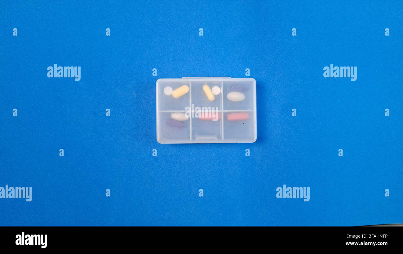 Organizer per pillole con compresse bianche e capsule su sfondo blu Foto Stock