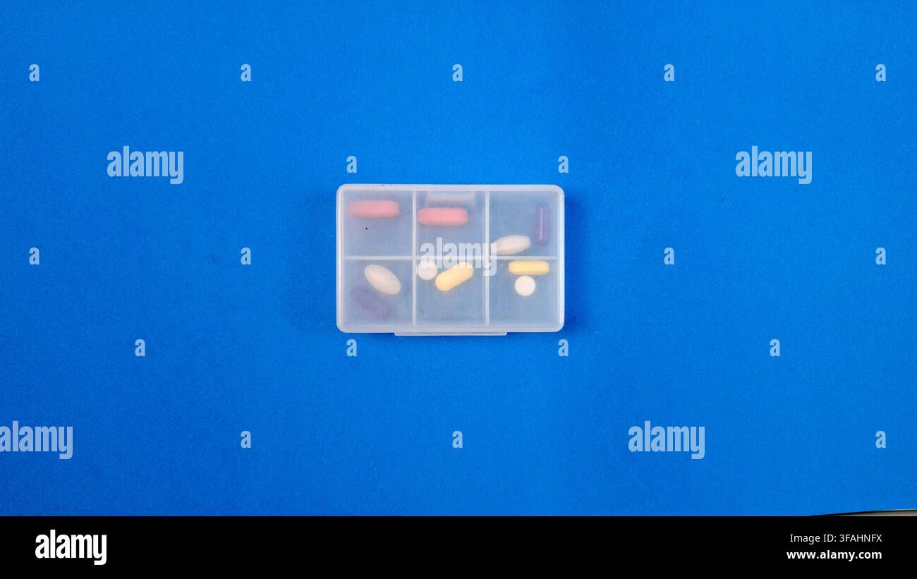 Organizer per pillole con compresse bianche e capsule su sfondo blu Foto Stock