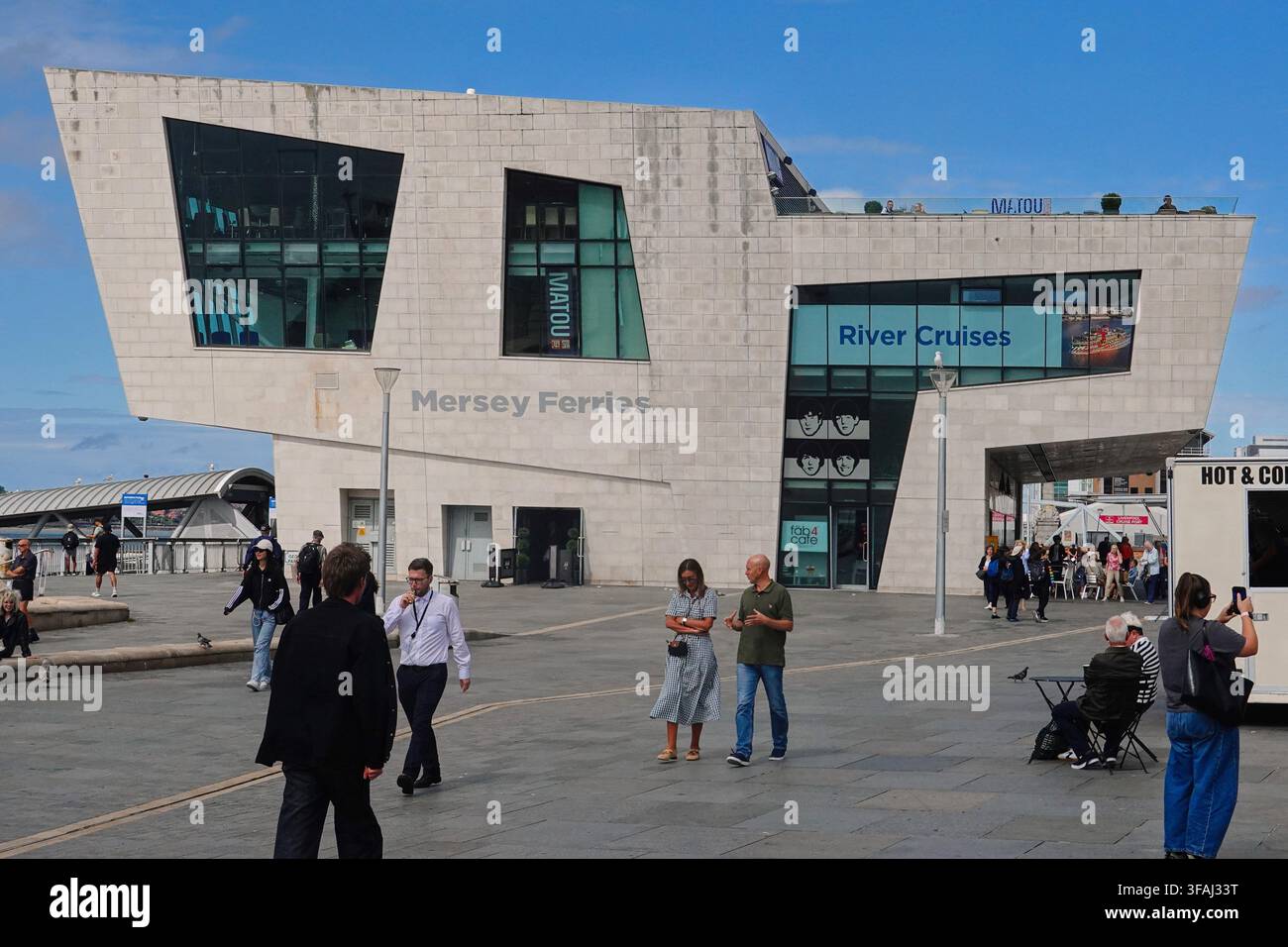 Pedoni che camminano nella piazza fuori dallo straordinario edificio moderno delle Mersey Ferries con il ristorante Matou e i cartelli River Cruises a Pier Head i Foto Stock