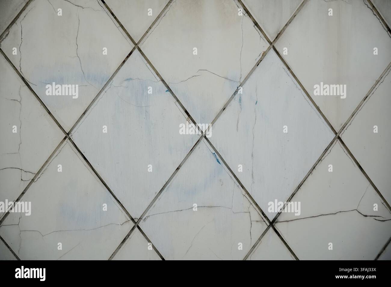 Primo piano di una vecchia parete piastrellata bianca con motivi quadrati diagonali. Le piastrelle in ceramica mostrano diverse crepe, danni e giunti stagionati. Foto Stock