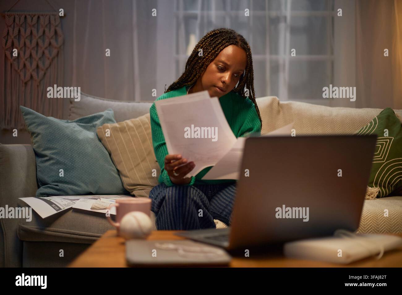 Donna nera che esamina documenti finanziari e fatture con un laptop a casa Foto Stock