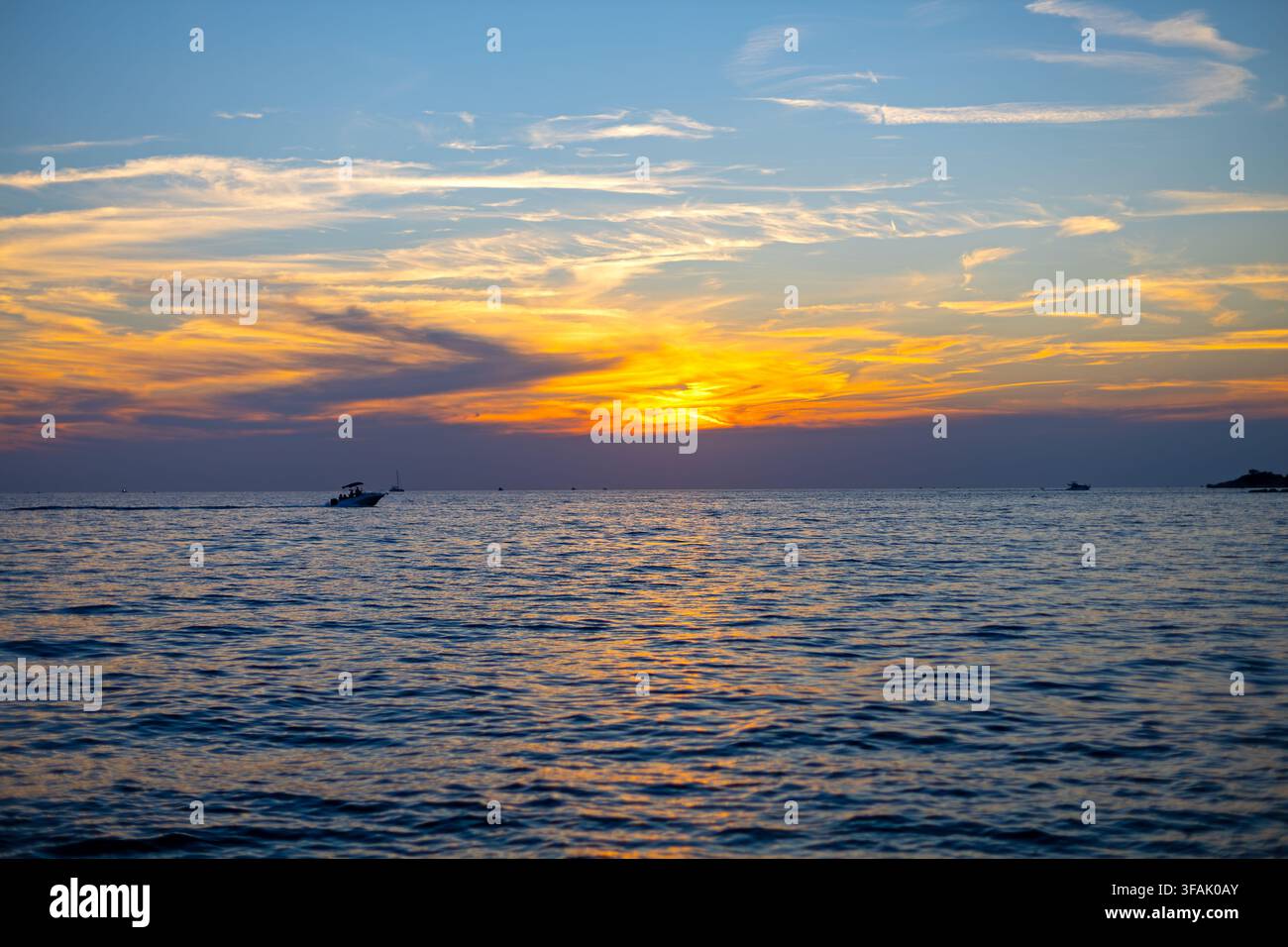 Tramonto dorato su un mare calmo con barche. Tramonto arancione su un mare calmo con nuvole stratificate, onde gentili, riflessi e piccole barche silouettate vicino alla riva Foto Stock
