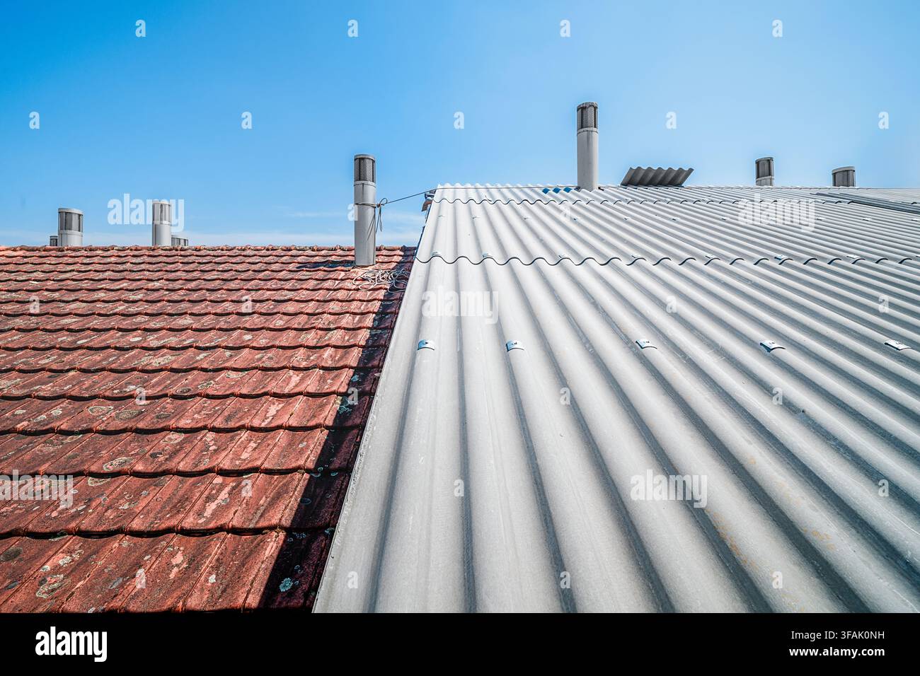 Piastrelle vecchie contrastanti e nuovi tetti ondulati contro un cielo blu Foto Stock