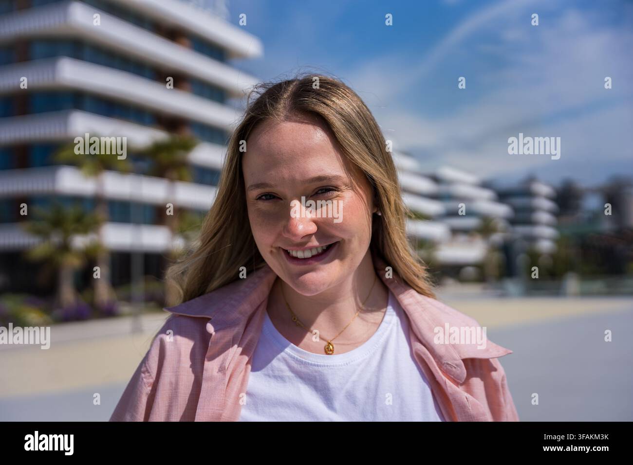 Giovane donna bionda sorridente che posa all'aperto in un quartiere moderno e soleggiato Foto Stock