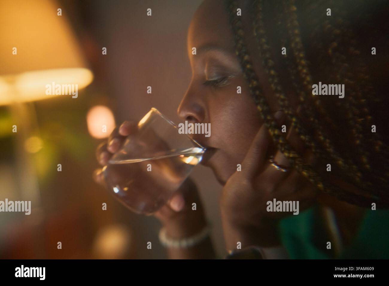 Donna nera che beve un bicchiere d'acqua per la routine di benessere serale Foto Stock