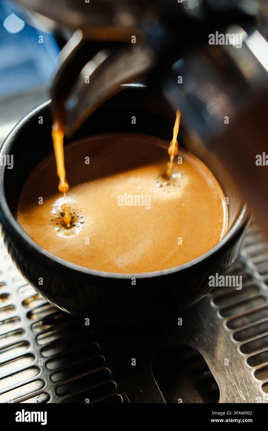 Estrarre doppio espresso che si riversa in una tazza di ceramica scura ripiena di spessa crema dorata. Scatto professionale di una macchina da caffè. Foto Stock
