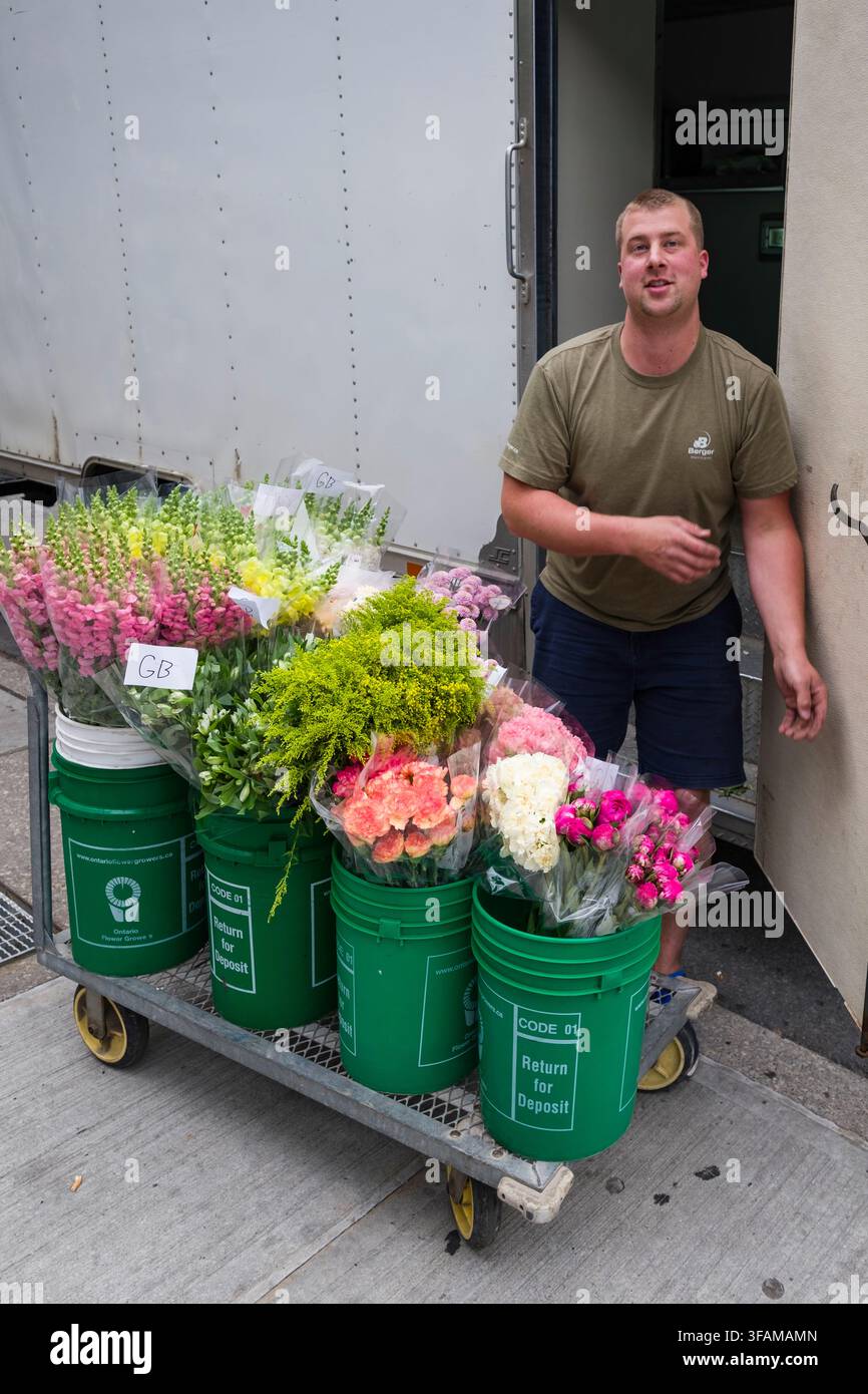 Catturato nel cuore di Toronto, un fioraio è in piedi accanto a un carrello pieno di fiori appena consegnati. Questi bouquet vivaci, probabilmente destinati Foto Stock
