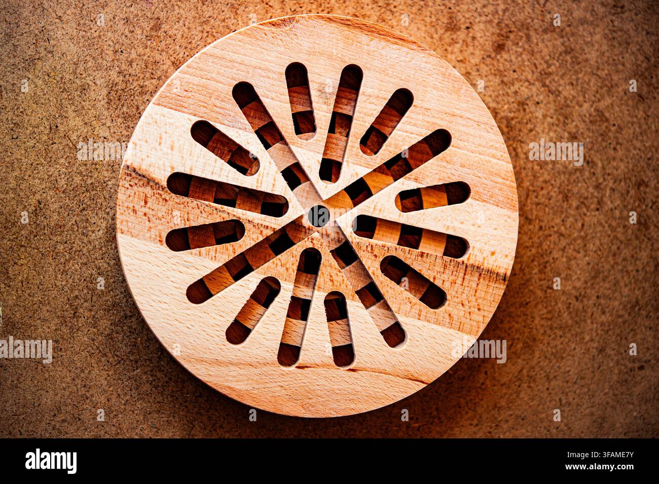 Vista dall'alto di un puzzle circolare a strati in legno con fessure radiali su una superficie marrone testurizzata, evidenziando l'artigianato geometrico e la venatura naturale del legno Foto Stock