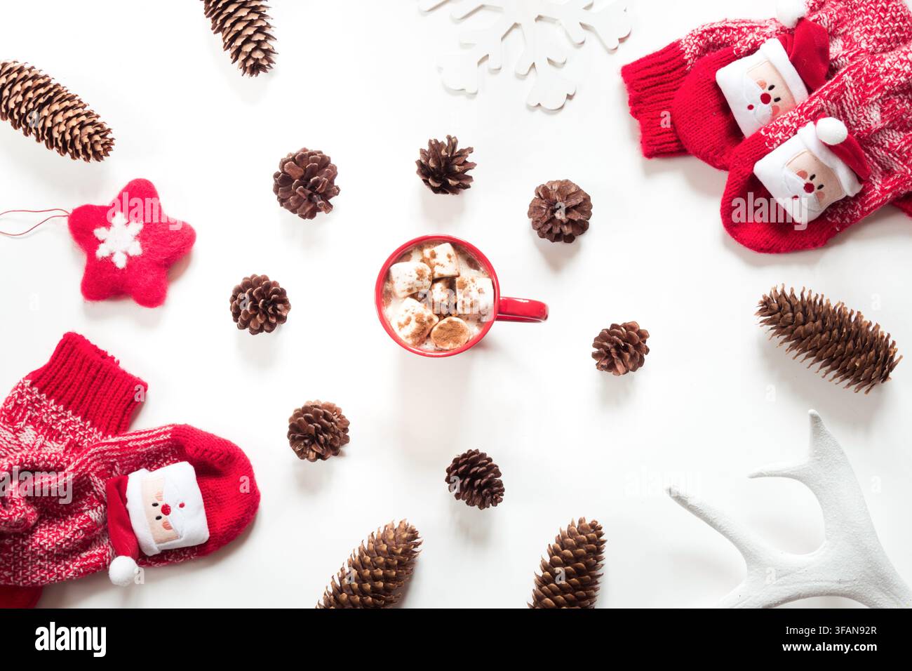 Cioccolata calda natalizia con marshmallow, cono, pelliccia bianca, stella di feltro rosso, calzini lavorati a maglia su sfondo bianco. Foto Stock