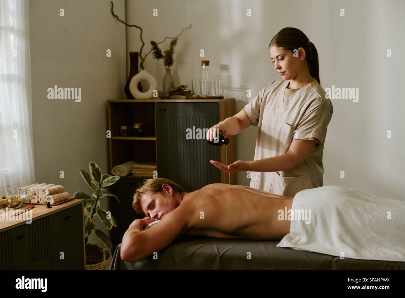 Terapeuta femminile che versa olio sulla schiena di un uomo durante un massaggio spa Foto Stock