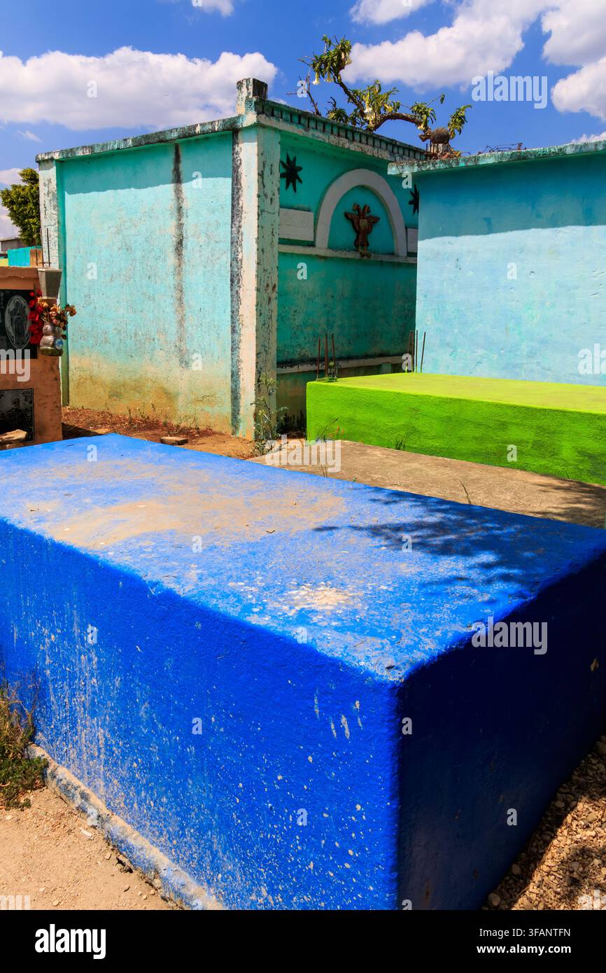 Tombe dipinte di blu brillante e verde in un piccolo cimitero sotto un cielo soleggiato con nuvole bianche, che mostrano le tradizioni locali di ricordo Foto Stock