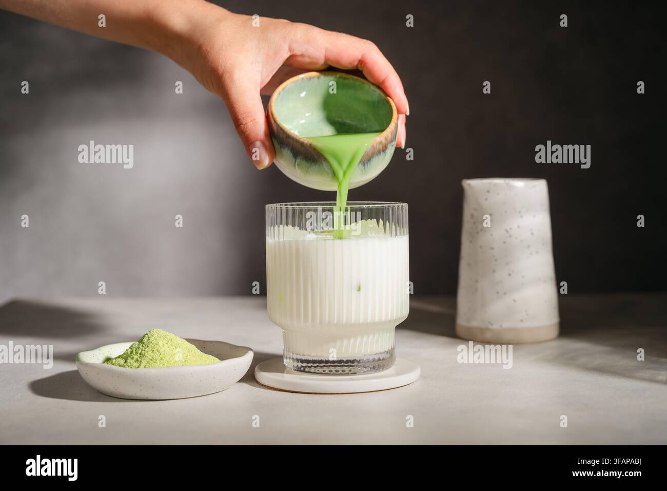 Mano che versa tè verde matcha nella latte fredda Foto Stock