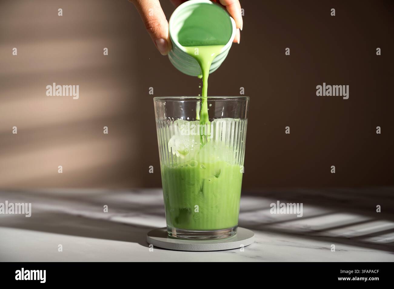 Mano che versa un latte freddo al tè verde matcha Foto Stock