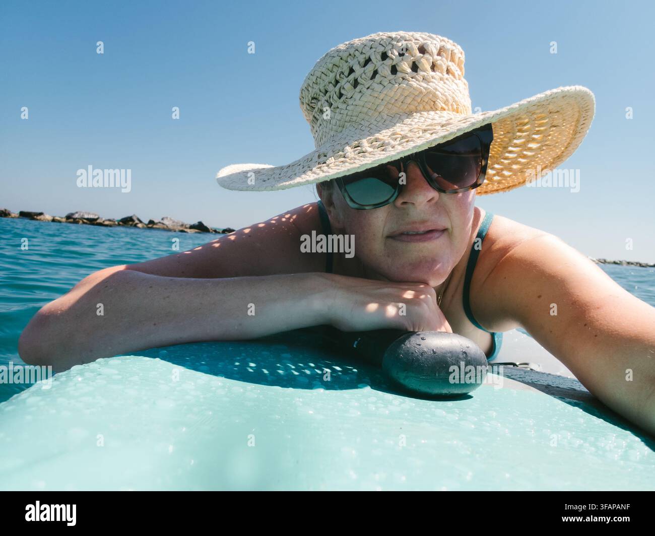 Donna con cappello da sole si rilassa sulla sua paddleboard Foto Stock