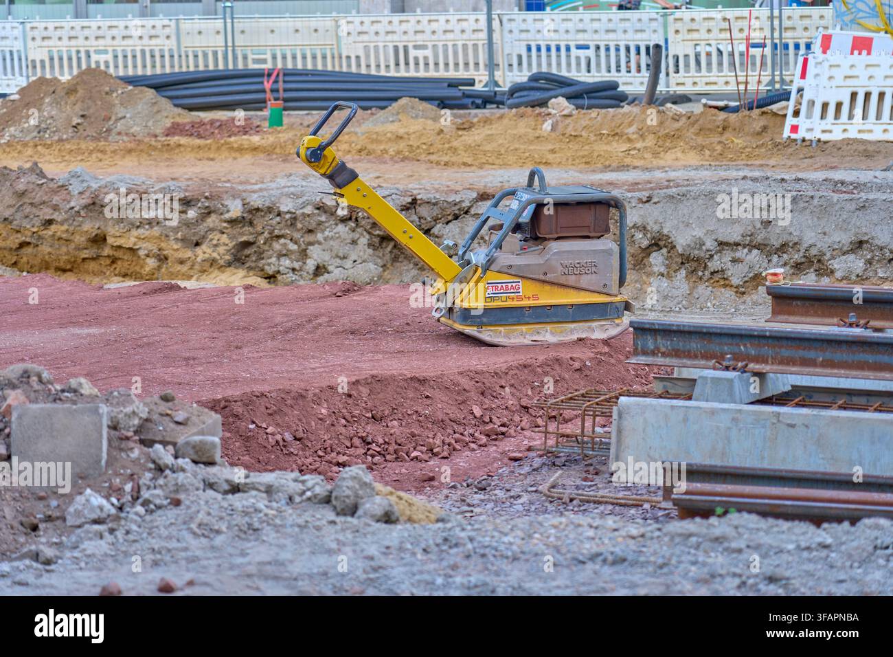 Compattatore a piastra giallo Wacker Neuson di Strabag stabilizza il terreno comunale, questo strumento ingegneristico rappresenta le forze invisibili della regolamentazione statale Foto Stock