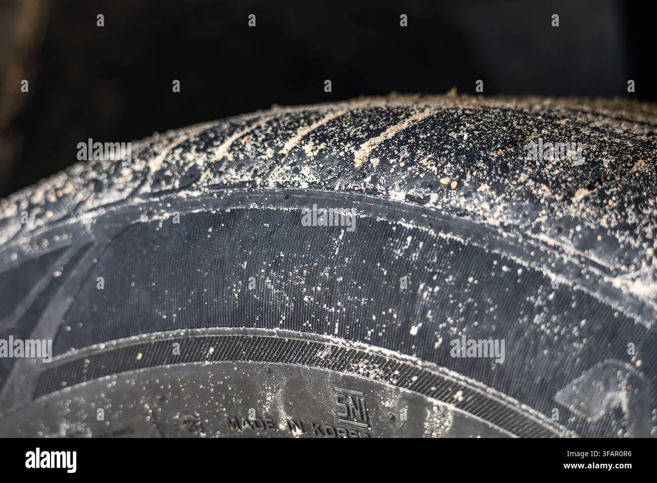 Fotografia drammatica in primo piano che mostra particelle di sabbia attaccate al battistrada e alla parete laterale di un pneumatico scuro di un'automobile. Foto Stock