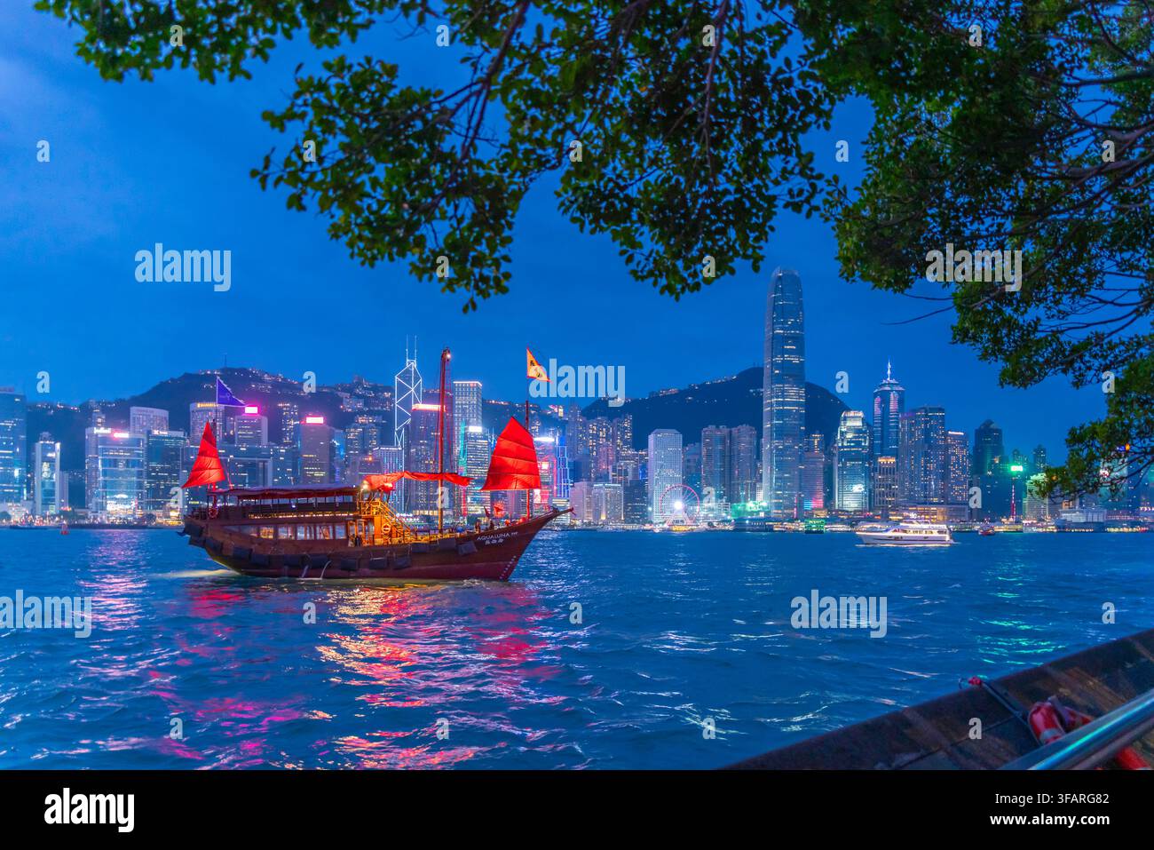 Vista dello skyline di Hong Kong e di una giunca a vela rossa da Kowloon al tramonto, Kowloon, Hong Kong, Cina Foto Stock