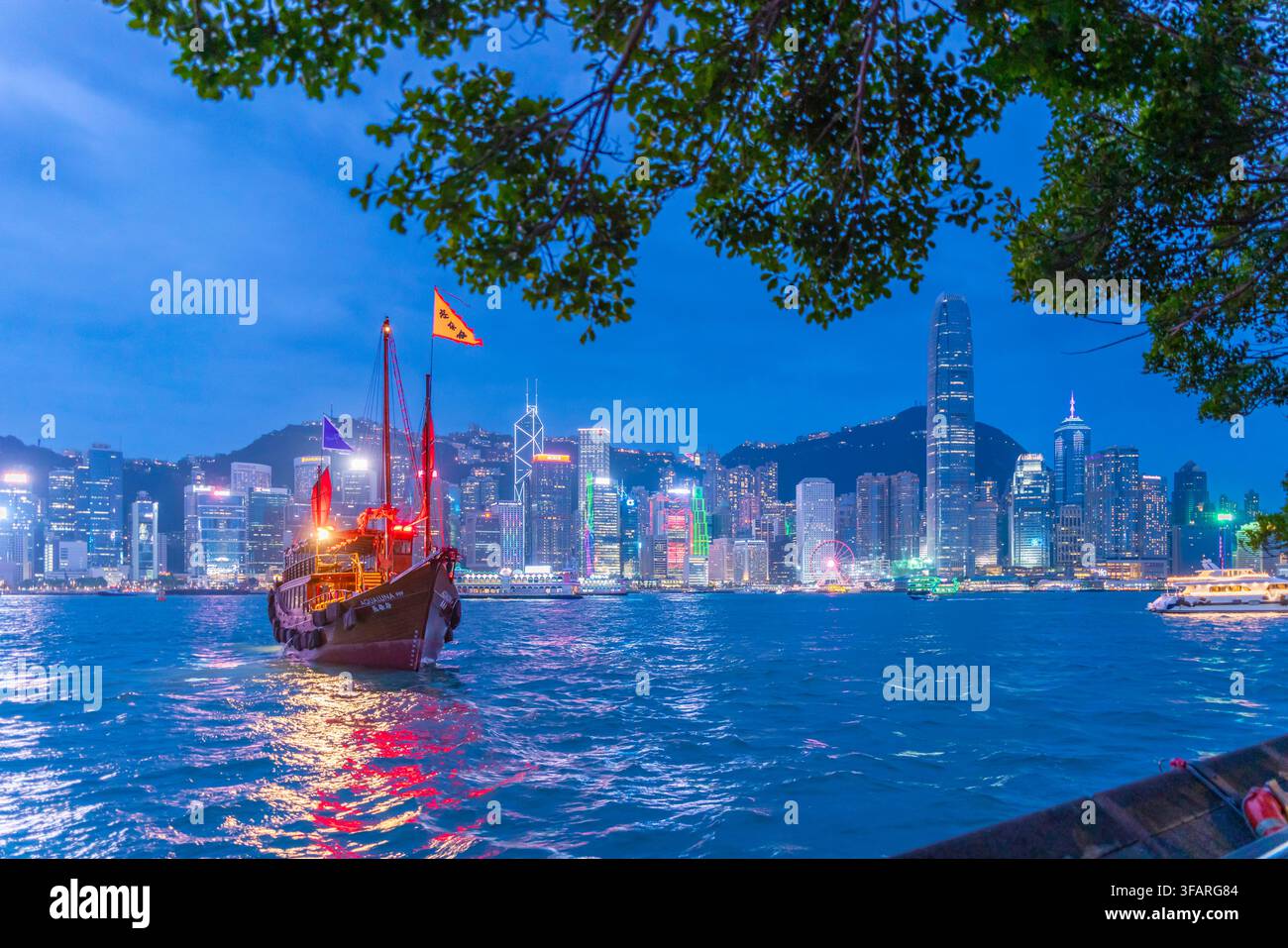 Vista dello skyline di Hong Kong e di una giunca a vela rossa da Kowloon al tramonto, Kowloon, Hong Kong, Cina Foto Stock