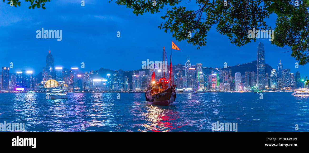 Vista dello skyline di Hong Kong e di una giunca a vela rossa da Kowloon al tramonto, Kowloon, Hong Kong, Cina Foto Stock