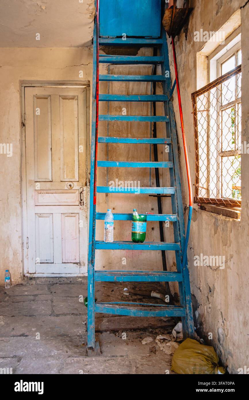 Scalinata in metallo blu all'interno di una stazione di funivia abbandonata e in decadenza con pareti scrostate e rifiuti sparsi a Chiatura, Georgia. Foto Stock