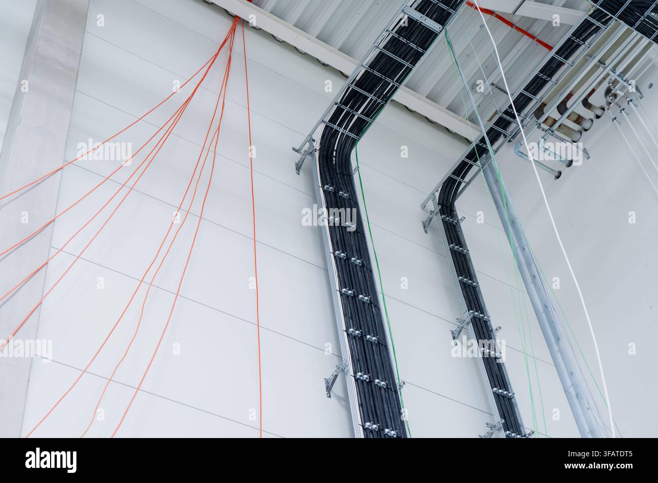 Scaffali per cavi sospesi che instradano linee di alimentazione strutturate su un muro di muratura simboleggiando ingegneria elettrica e distribuzione di energia industriale Foto Stock