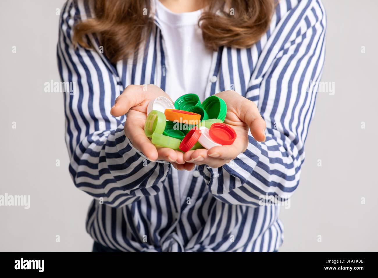 Persona irriconoscibile che tiene tappi di bottiglia di plastica colorati, ambientazione interna, concetto di riciclaggio Foto Stock