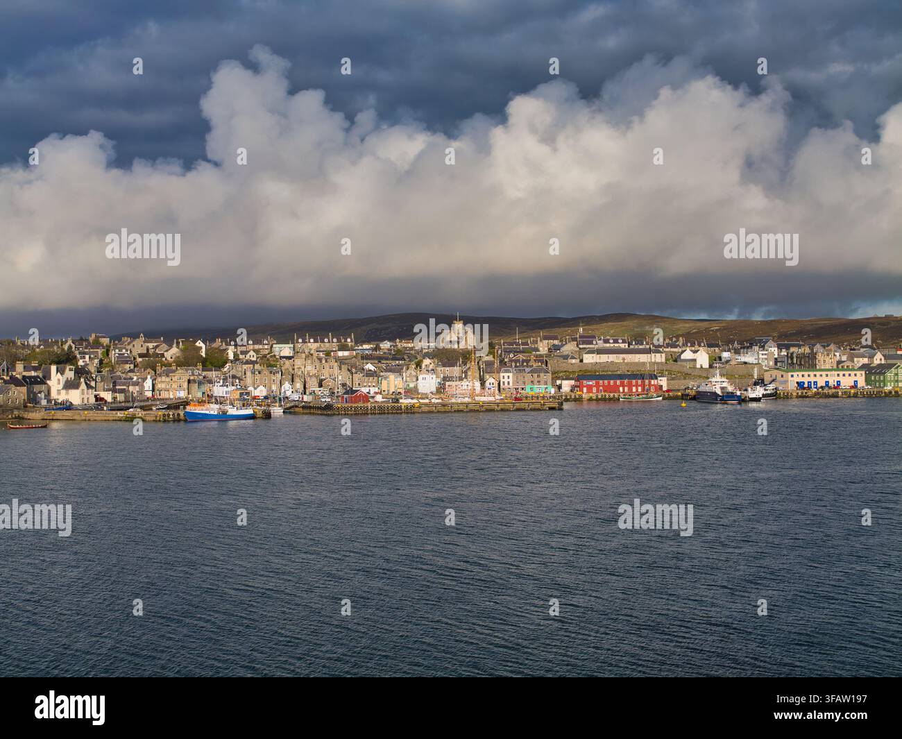 Shetland, UK – 18 maggio 2026: La luce del mattino illumina il lungomare di Lerwick nelle Shetland, UK, sotto drammatiche nuvole di tempesta, con barche da pesca e edifici colorati del porto Foto Stock