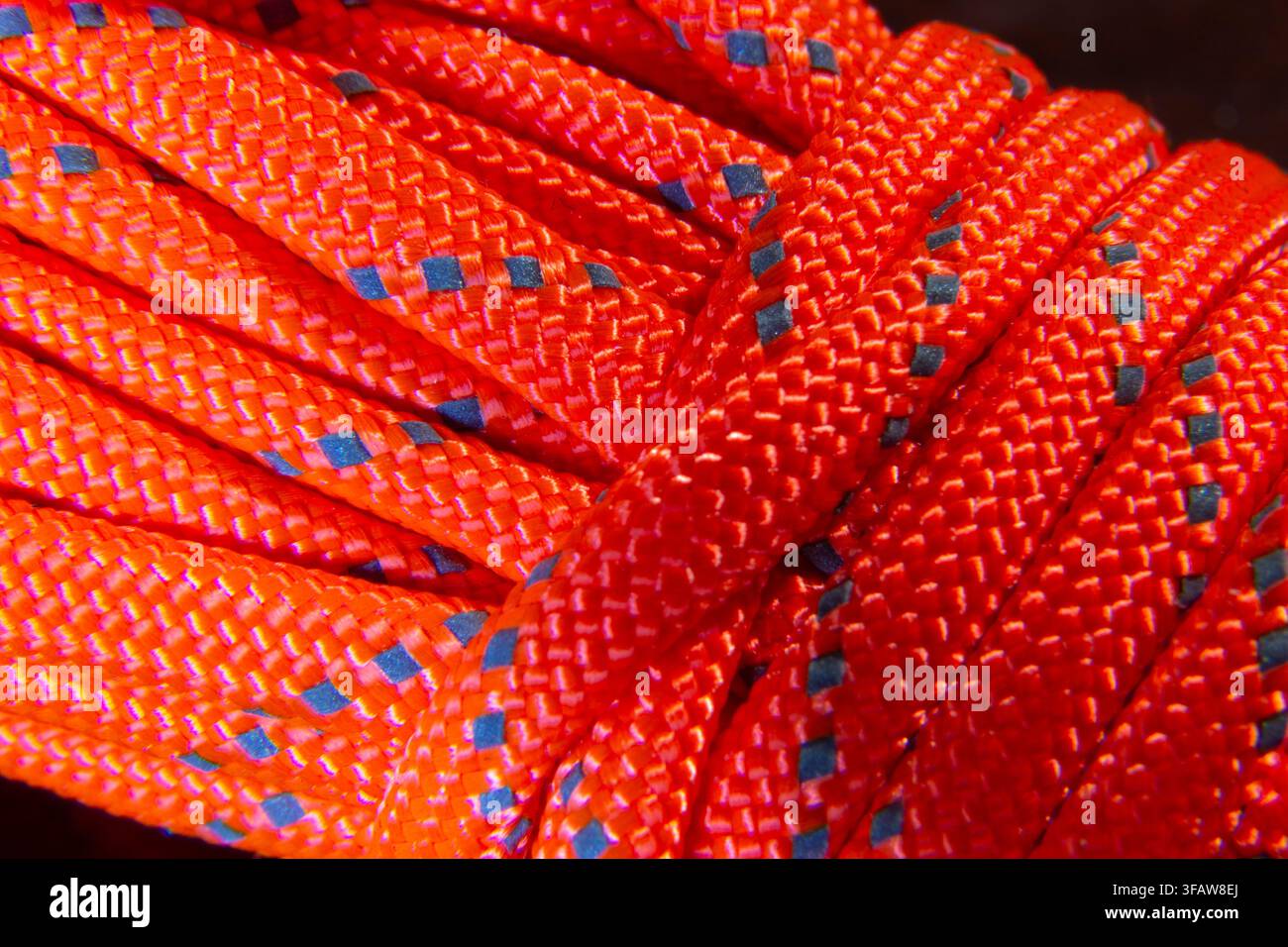Vista macro astratta di una paracord arancione strettamente intrecciata che forma una trama e un motivo ripetitivo intricato Foto Stock