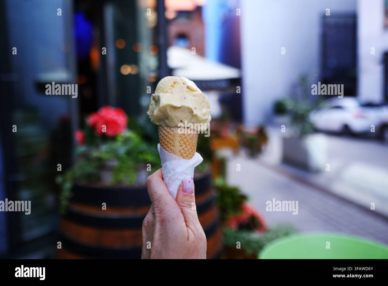 Mano che tiene un cucchiaio di gelato cremoso in una cono di waffle all'aperto in una giornata estiva soleggiata. Foto Stock
