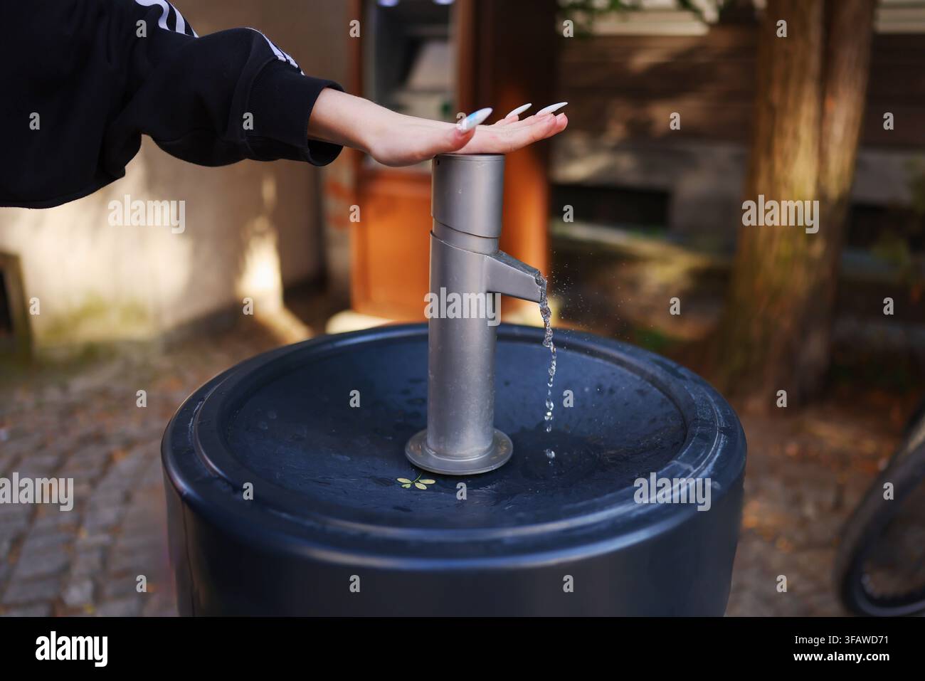 Donna che utilizza una fontana di acqua potabile pubblica all'aperto, preme la pompa mentre l'acqua fresca scorre dal rubinetto. Foto Stock