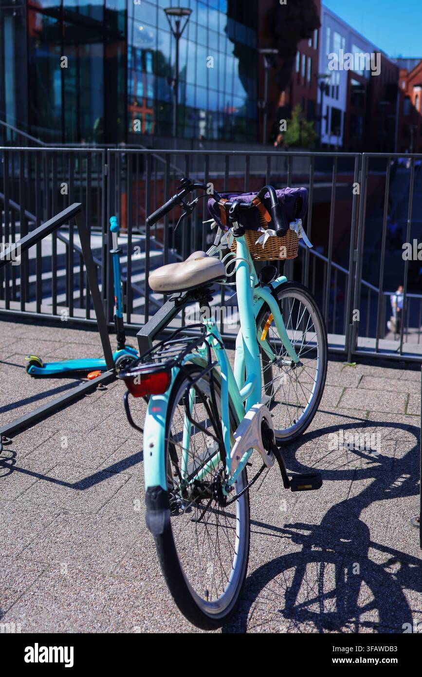 Bicicletta da città turchese con cestino di vimini parcheggiata all'aperto vicino a edifici urbani moderni in una giornata soleggiata. Foto Stock