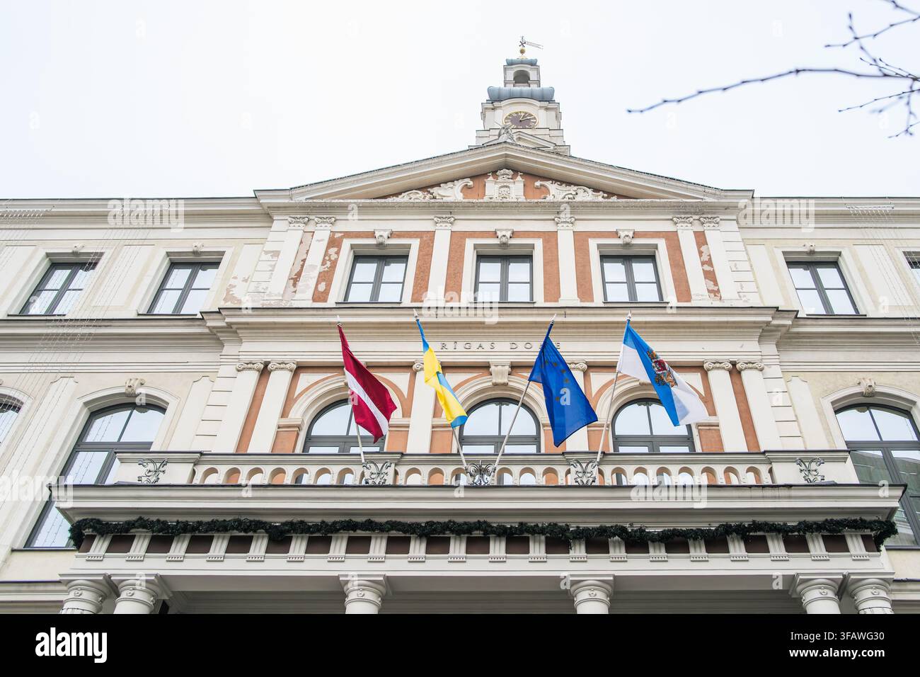 Il carattere municipale attraverso le bandiere emerge su una facciata classica di Riga dove le bandiere lettone, cittadine ed europee segnano l'identità civica per il governo. Foto Stock